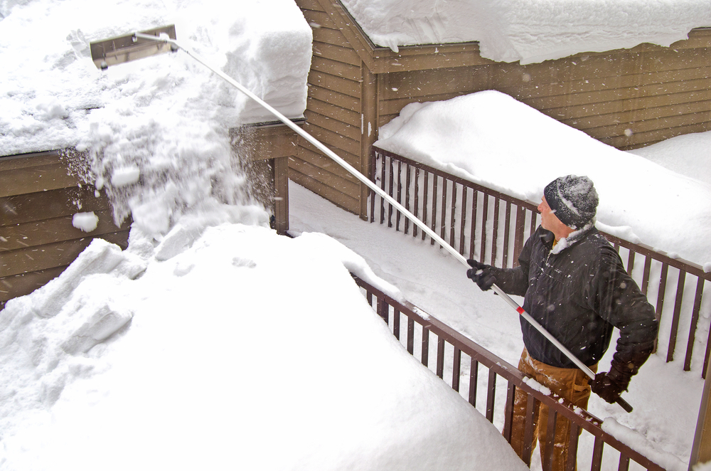 a man using a roof rake to get snow off of his roof