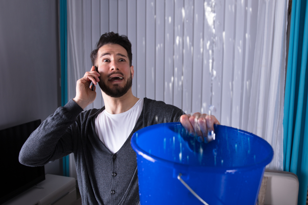 a man holding a bucket to catch leaking water